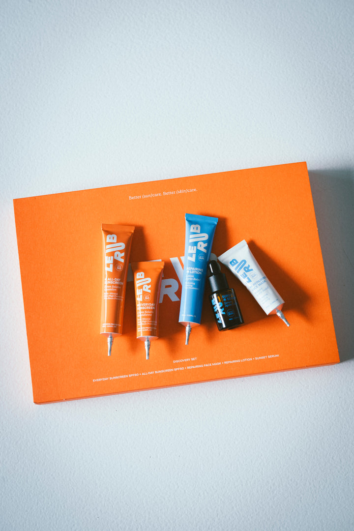 Five Le Rub Products (Everyday Sunscreen SPF50, All Day Sunscreen SPF50, Repairing Lotion, Sunset Serum, Repairing Face Mask) on top of Orange Discovery Set Case