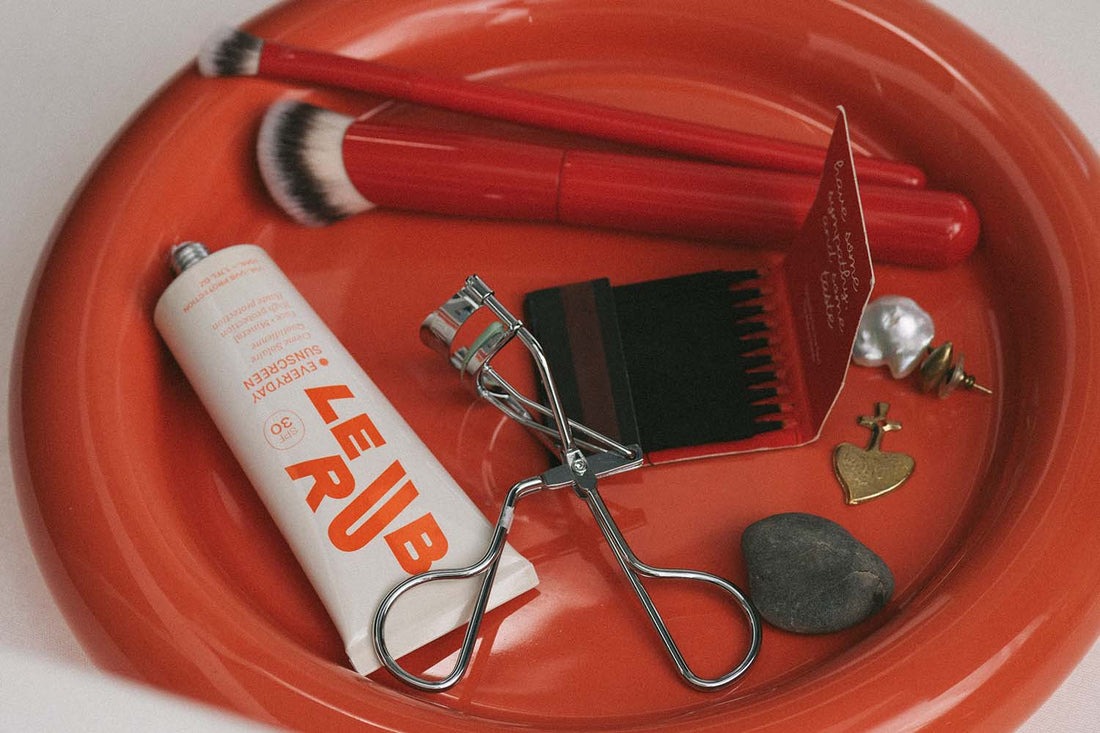 red tray with makeup brushes, earrings, eyelash curler and Le Rub Everyday Sunscreen