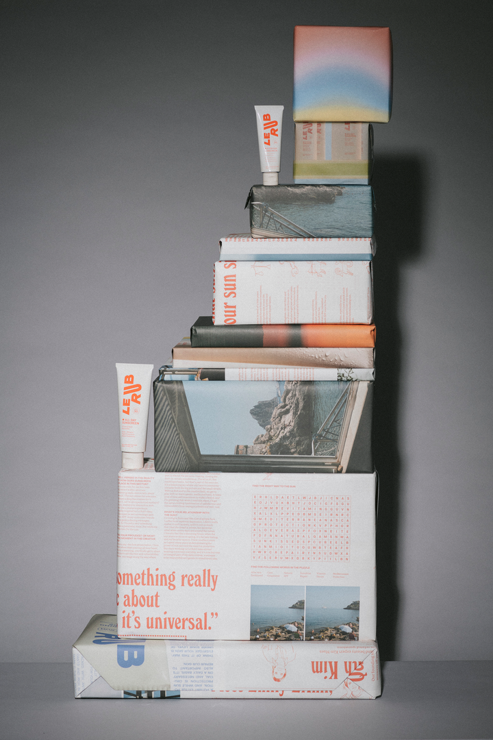 Stack of books and magazines on a gray background with Le Rub Everyday Sunscreen SPF30 and Le Rub All-day Sunscreen SPF30